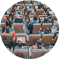 Circular photo with view into a full conference hall with many people seated in rows, all facing forward.