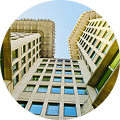 Circular photo of a tall building with symmetrical window patterns, taken from a low-angle perspective looking up at the sky.